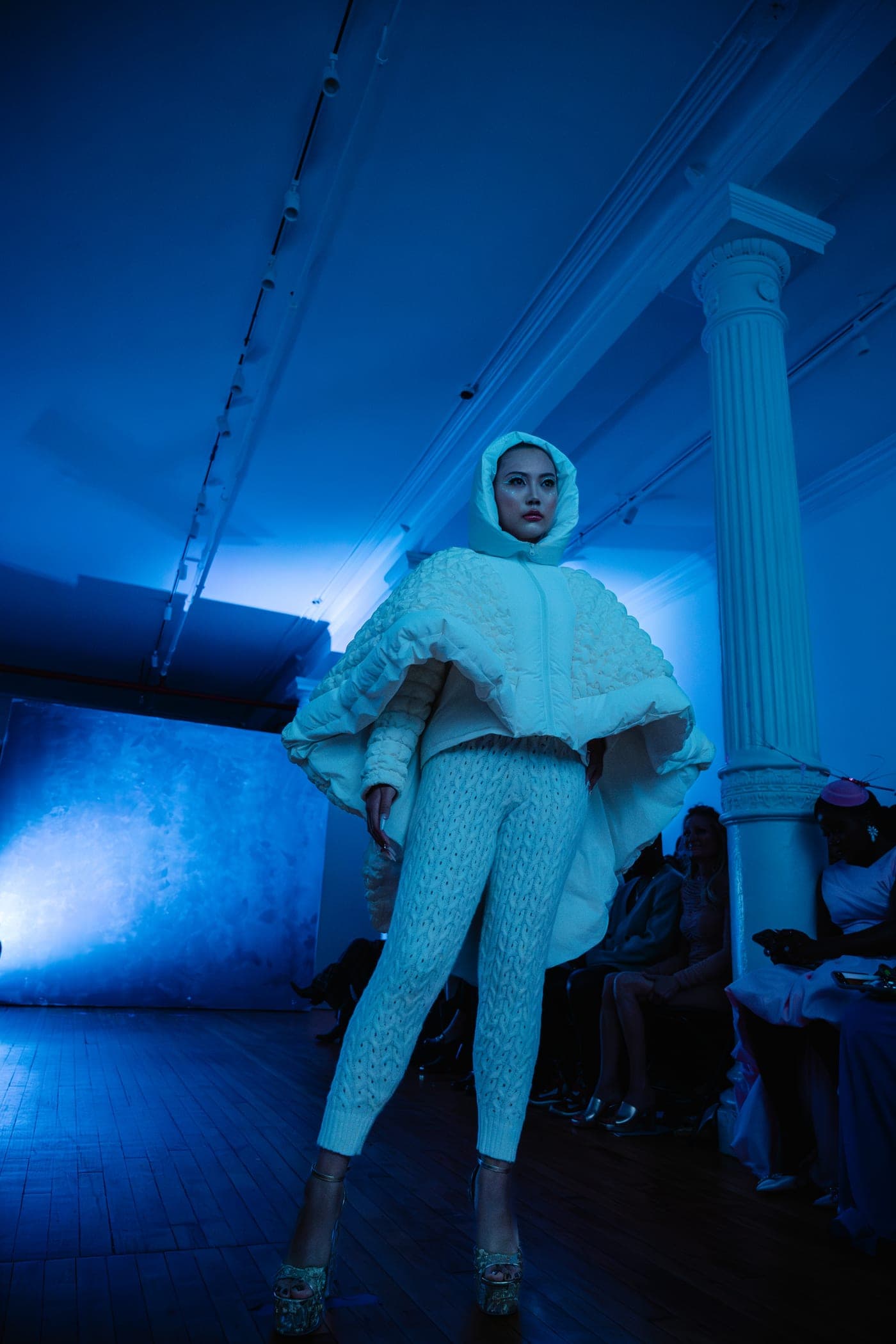 A hooded cream puffer with a wide flared hem, worn over cable-knit leggings, mid-walk on the runway.